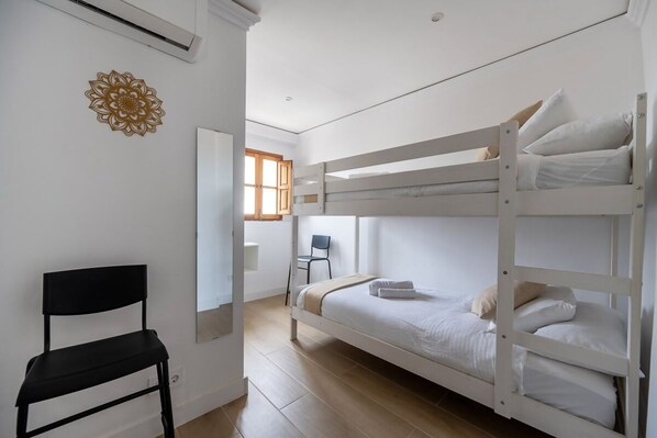 A bunk bed room with a black chair, a wall-mounted air conditioner, and a window with wooden shutters.
