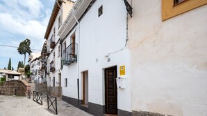 Uma rua estreita com edifícios brancos, uma porta de madeira e uma placa amarela.