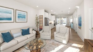 A modern living room with a beige sofa, two armchairs, a glass coffee table, and artwork on the walls.