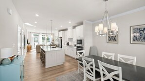 A modern kitchen with white cabinets, a central island, and a dining area with white chairs.
