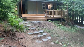 A cabin with a wooden deck, a staircase, and a stone pathway leading to the entrance.