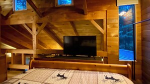 A wooden cabin with a bed, a television, and two windows with blue lighting.