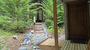 A wooden deck leading to a cabin with a green roof, surrounded by a forest.