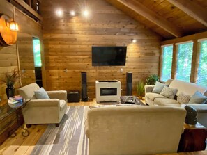 A log cabin interior with a fireplace, sofa, TV, and windows.