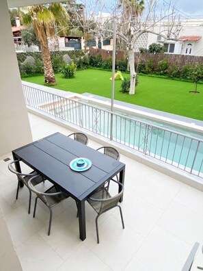 Ein Balkon mit Tisch und Stühlen, der einen Swimmingpool und einen gepflegten Garten überblickt.