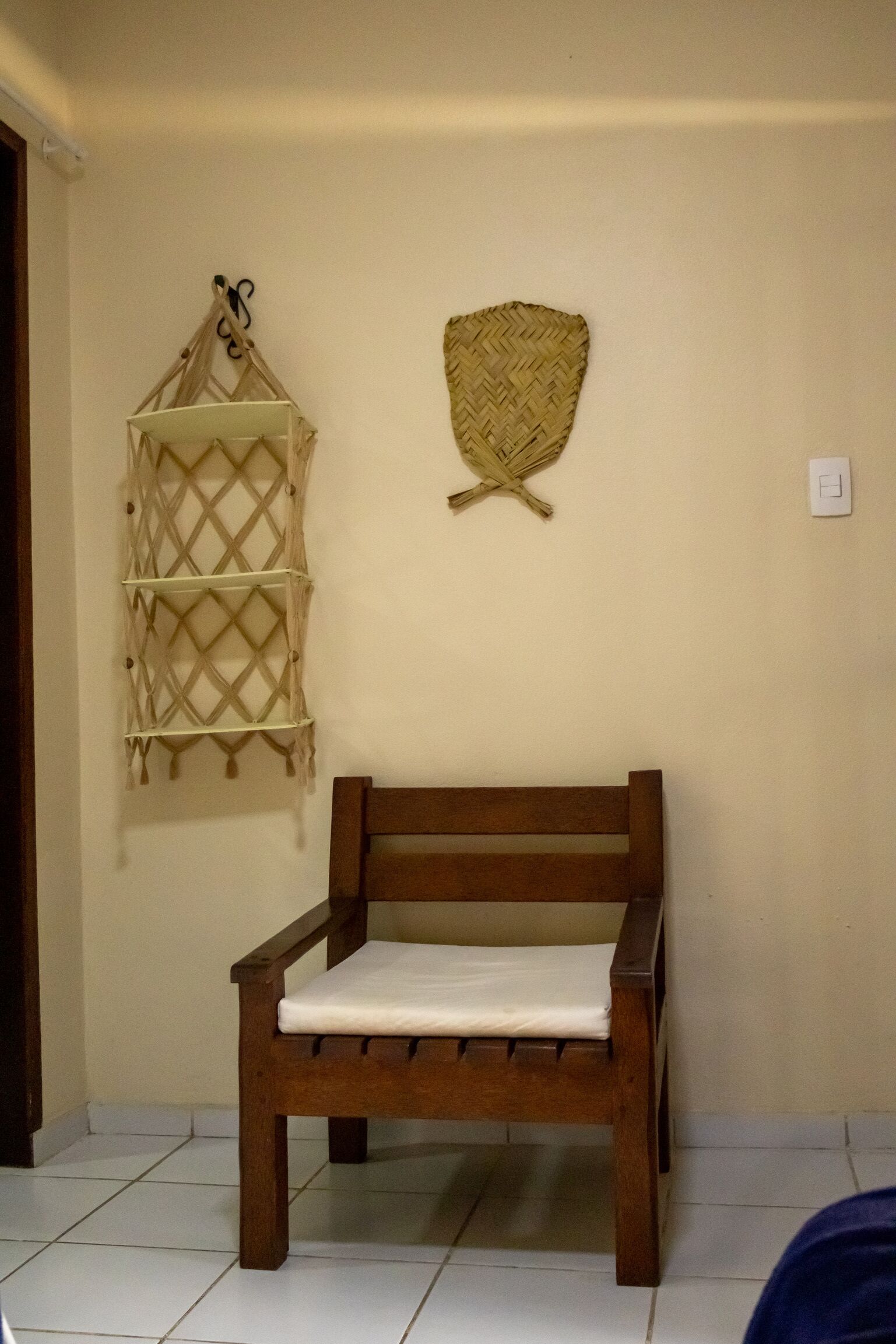 A wooden bench with a cushion against a wall, a woven wall hanging, and a lattice shelf.