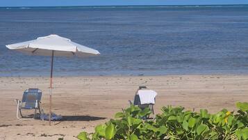 Di pantai, pasir putih, kursi berjemur, dan payung pantai
