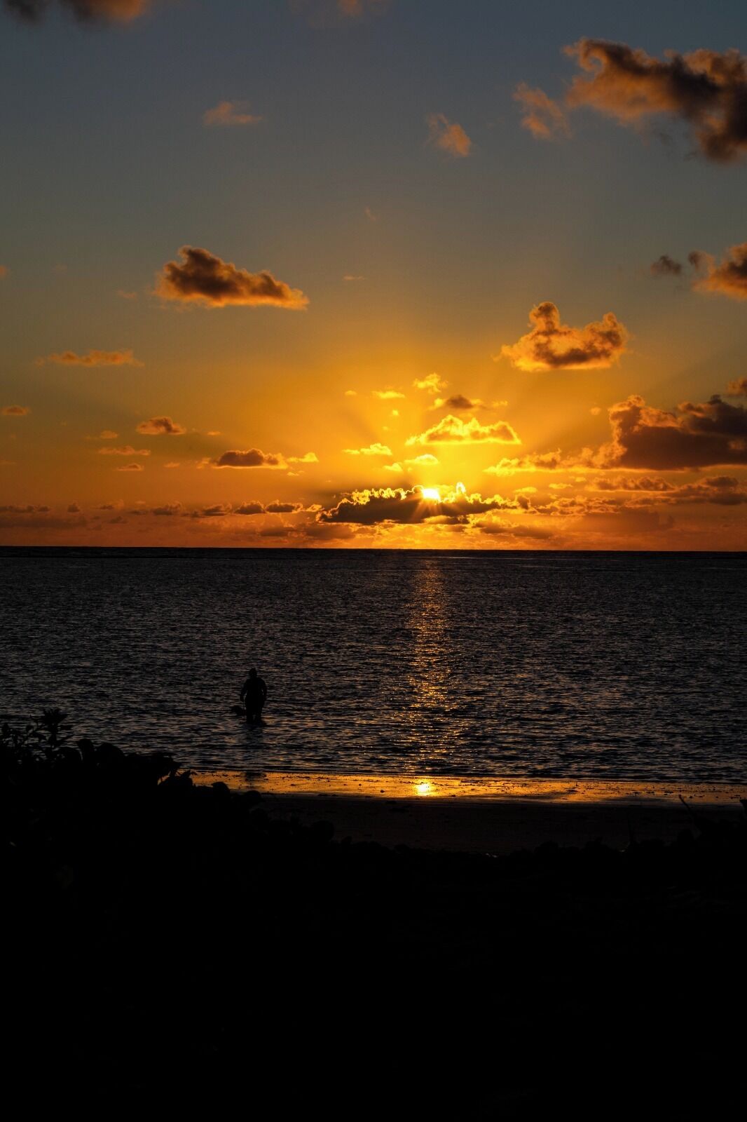 A sunset over a body of water with a silhouette of a person standing in the foreground.