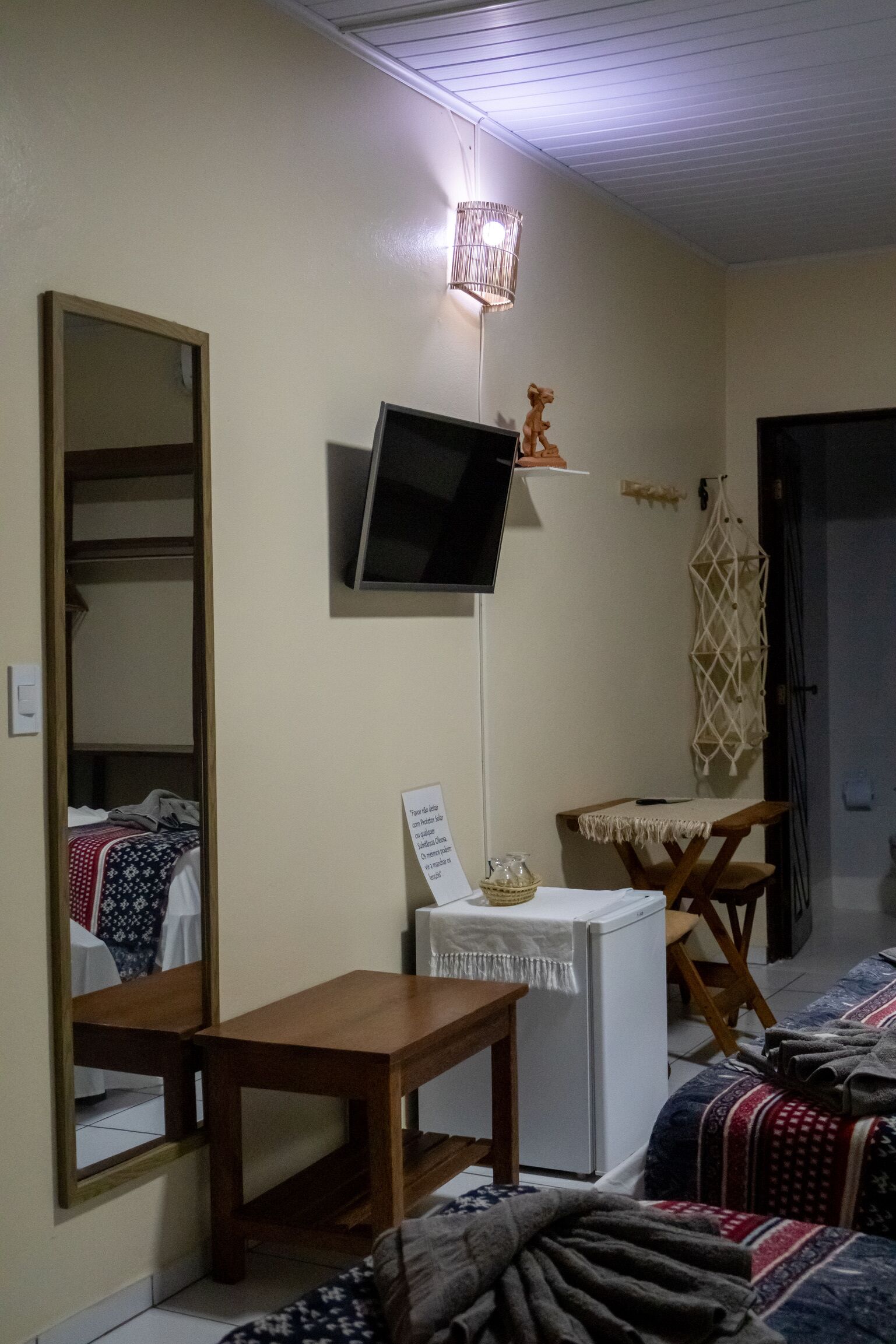 A bedroom with a bed, a bedside table, a mirror, a TV, and a small desk.