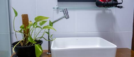Un baño con un lavamanos blanco, una planta en maceta y un secador rojo sobre una estantería.