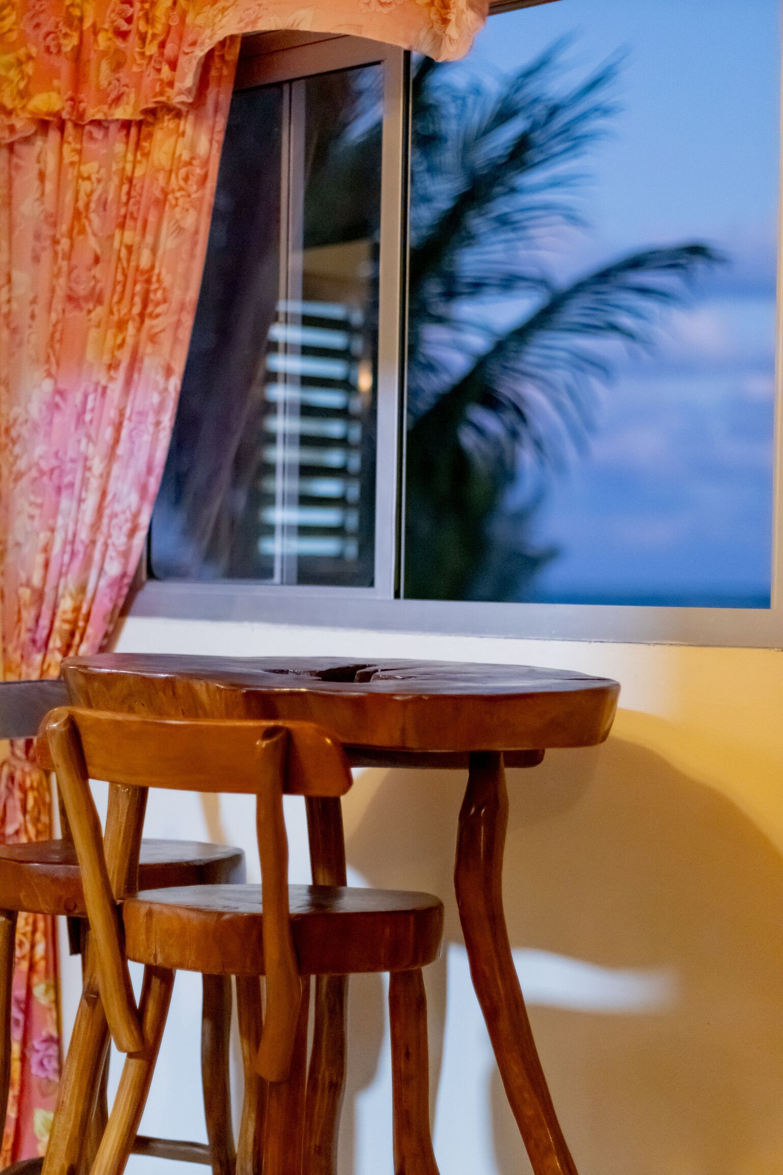 A wooden table and chairs near a window with a view of palm trees.
