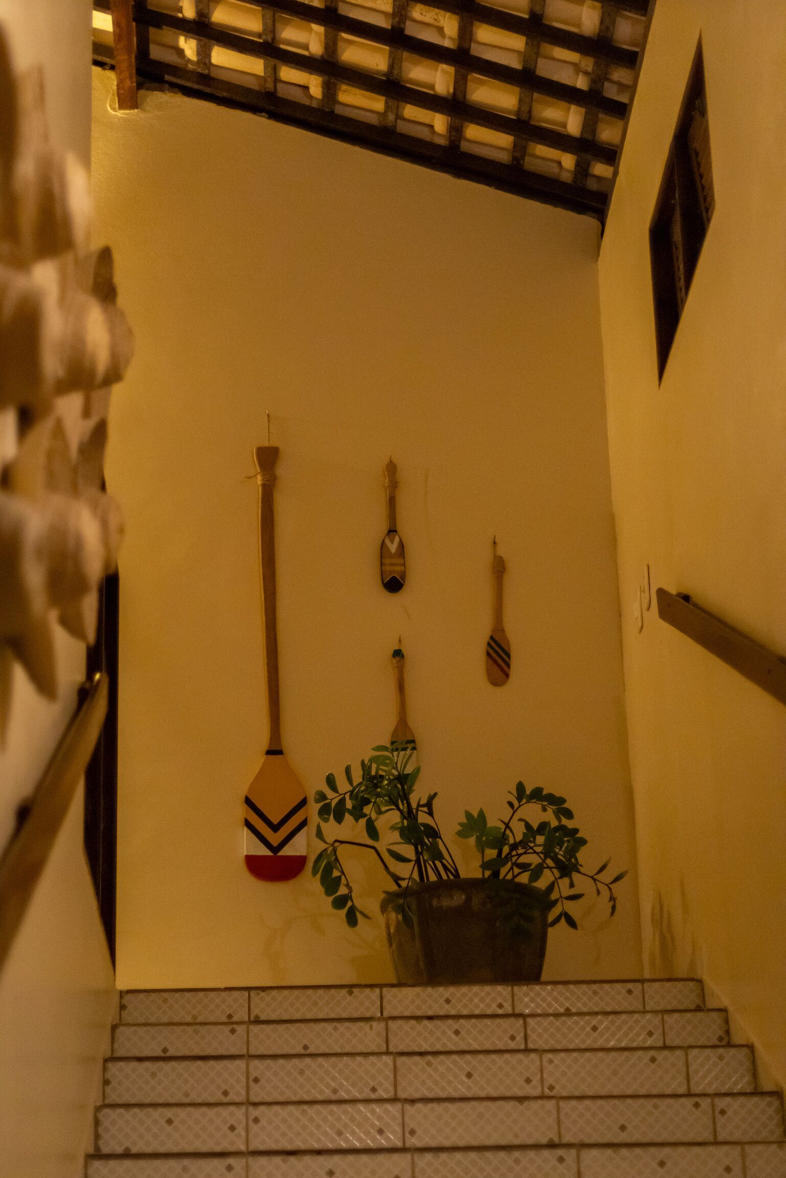 Een trap met een bloempot onderaan, een houten leuning en een muur met decoratieve objecten.