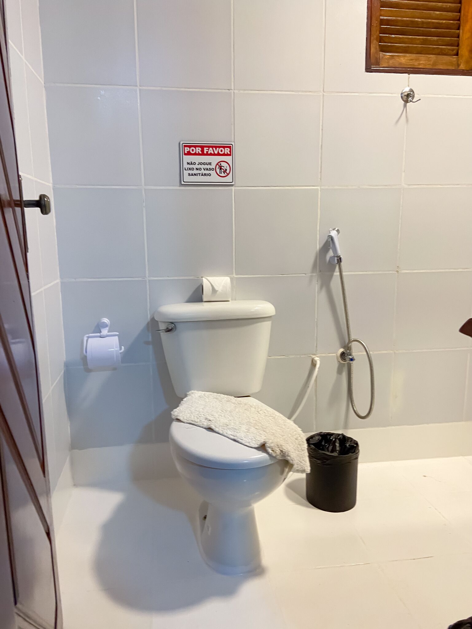 A bathroom with a toilet, a shower, and a trash bin.