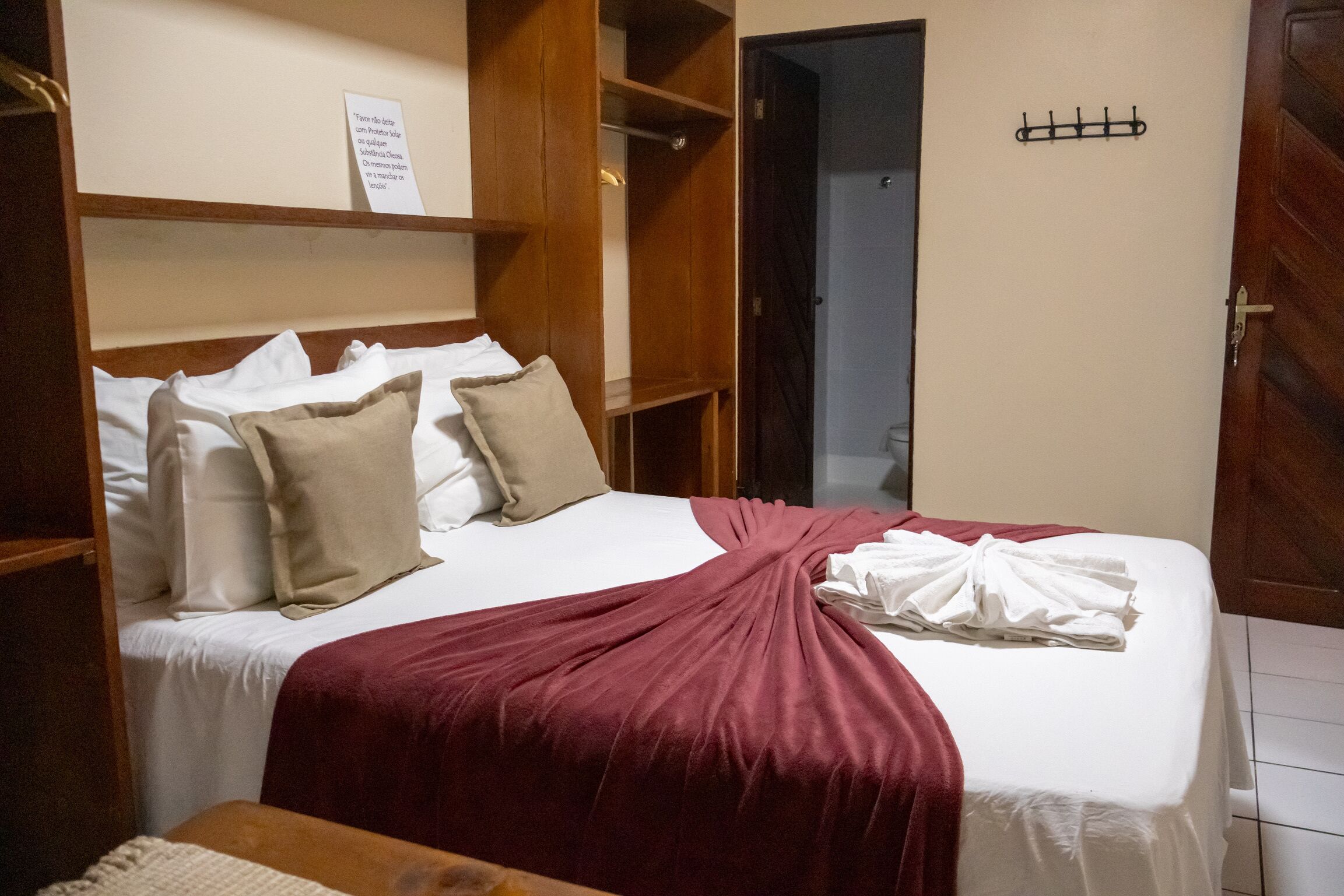 A neatly made bed with a red blanket, a wooden wardrobe, and a sign on the wall.