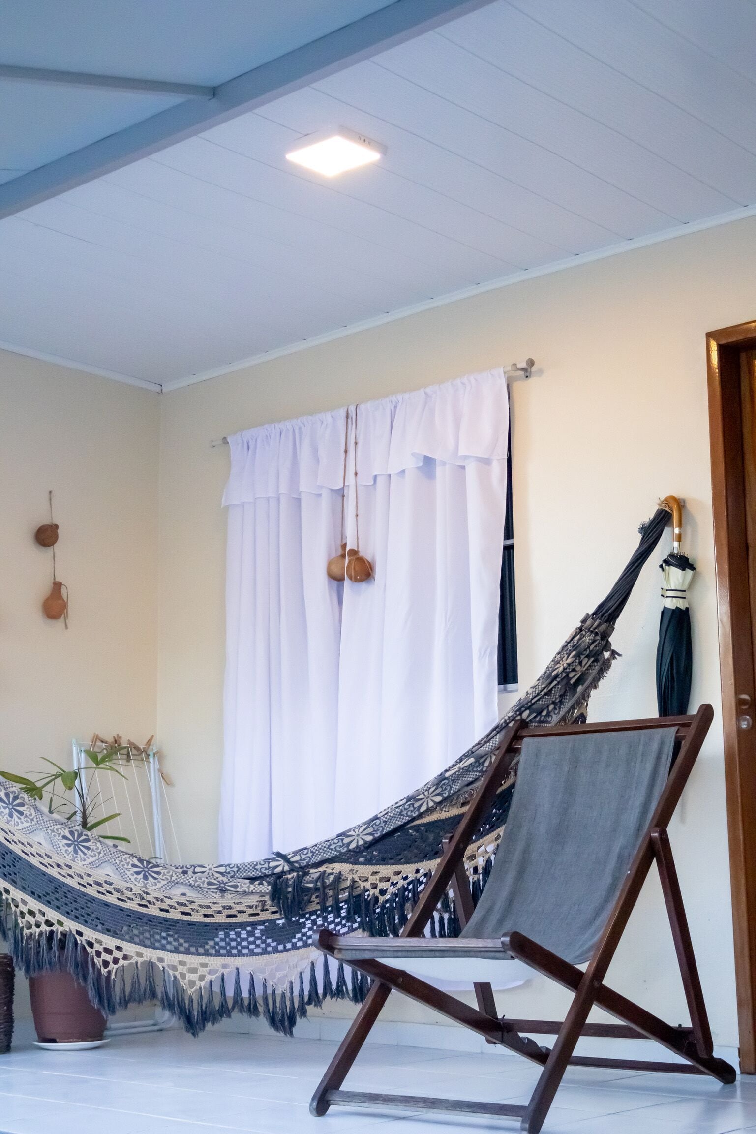 A hammock chair and a hammock with a decorative pattern, a potted plant, and a wooden door.