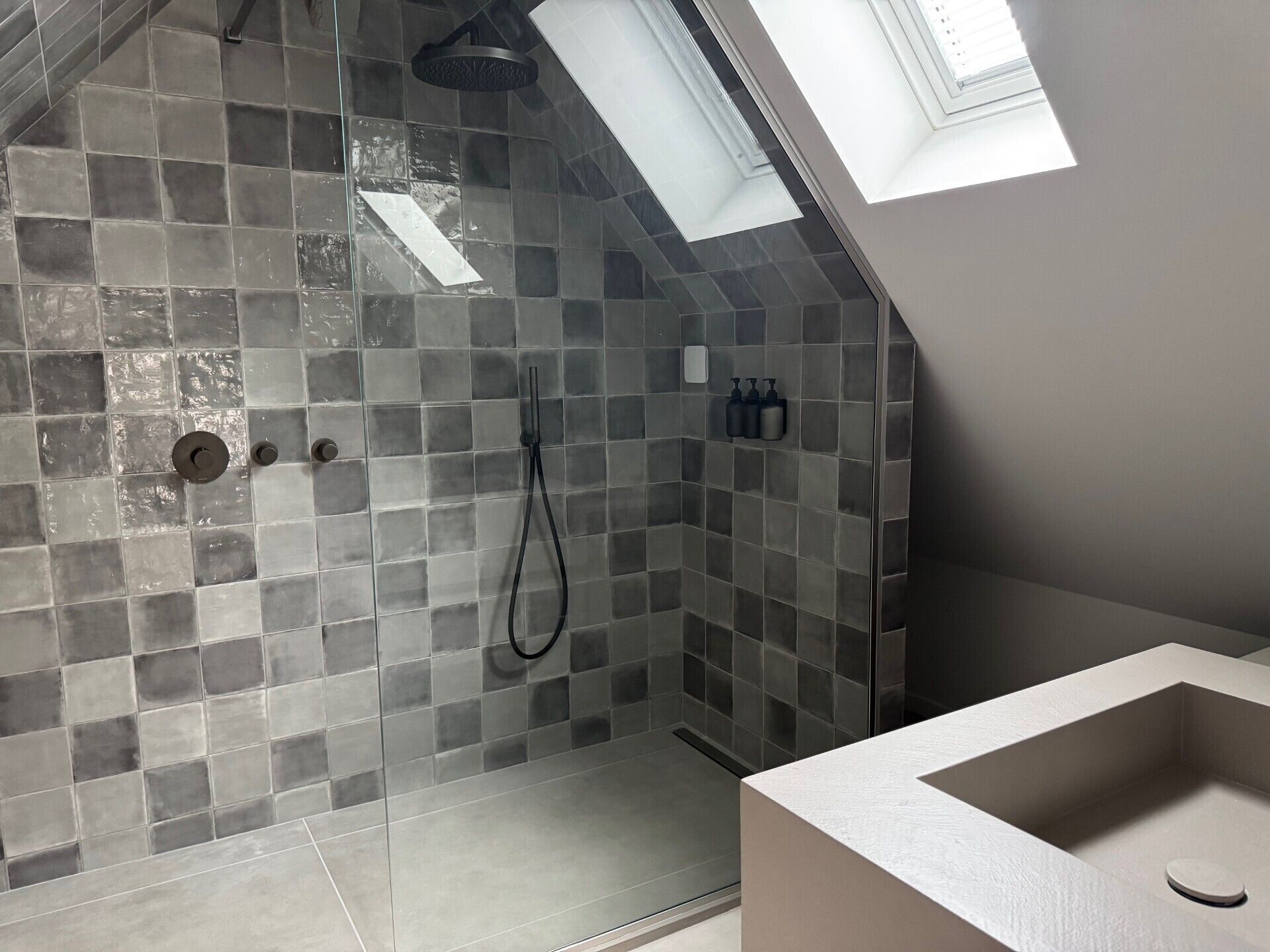 A modern bathroom with a shower area featuring gray mosaic tiles, a visible showerhead, and a skylight above.