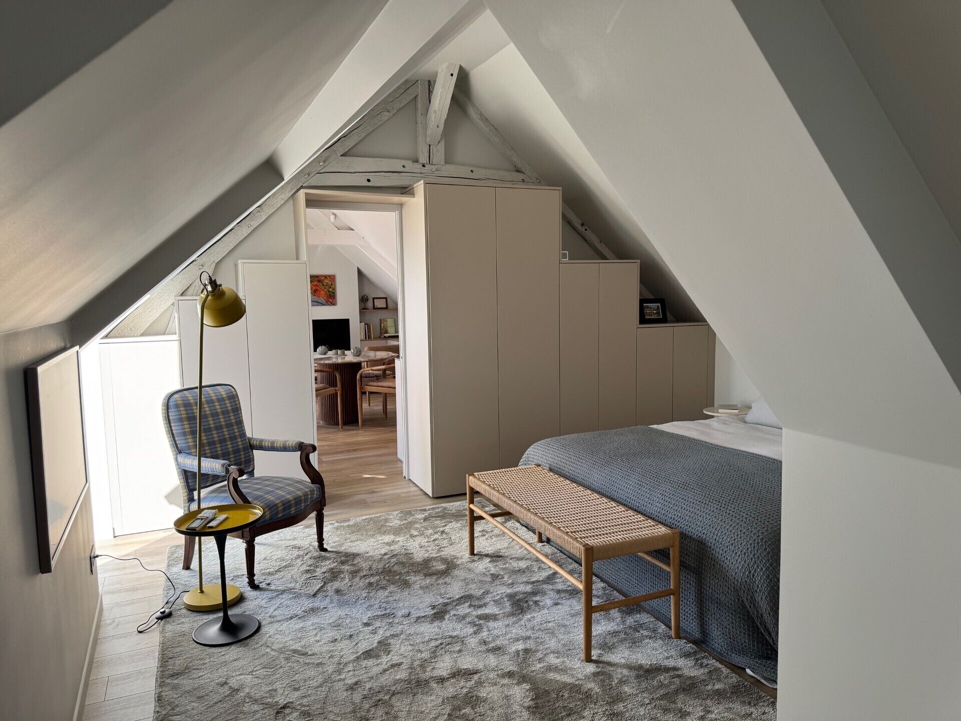 Une chambre mansardée chaleureuse avec un plafond en pente, un lit, une chaise, une petite table et un banc.