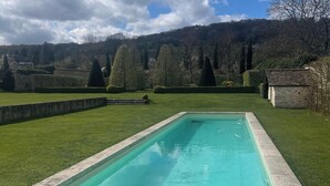 A rectangular swimming pool with a stone edge, surrounded by a grassy lawn and a stone wall. - Exceptional country apartment with pool, jacuzzi and sauna (La Chapelle-Longueville)