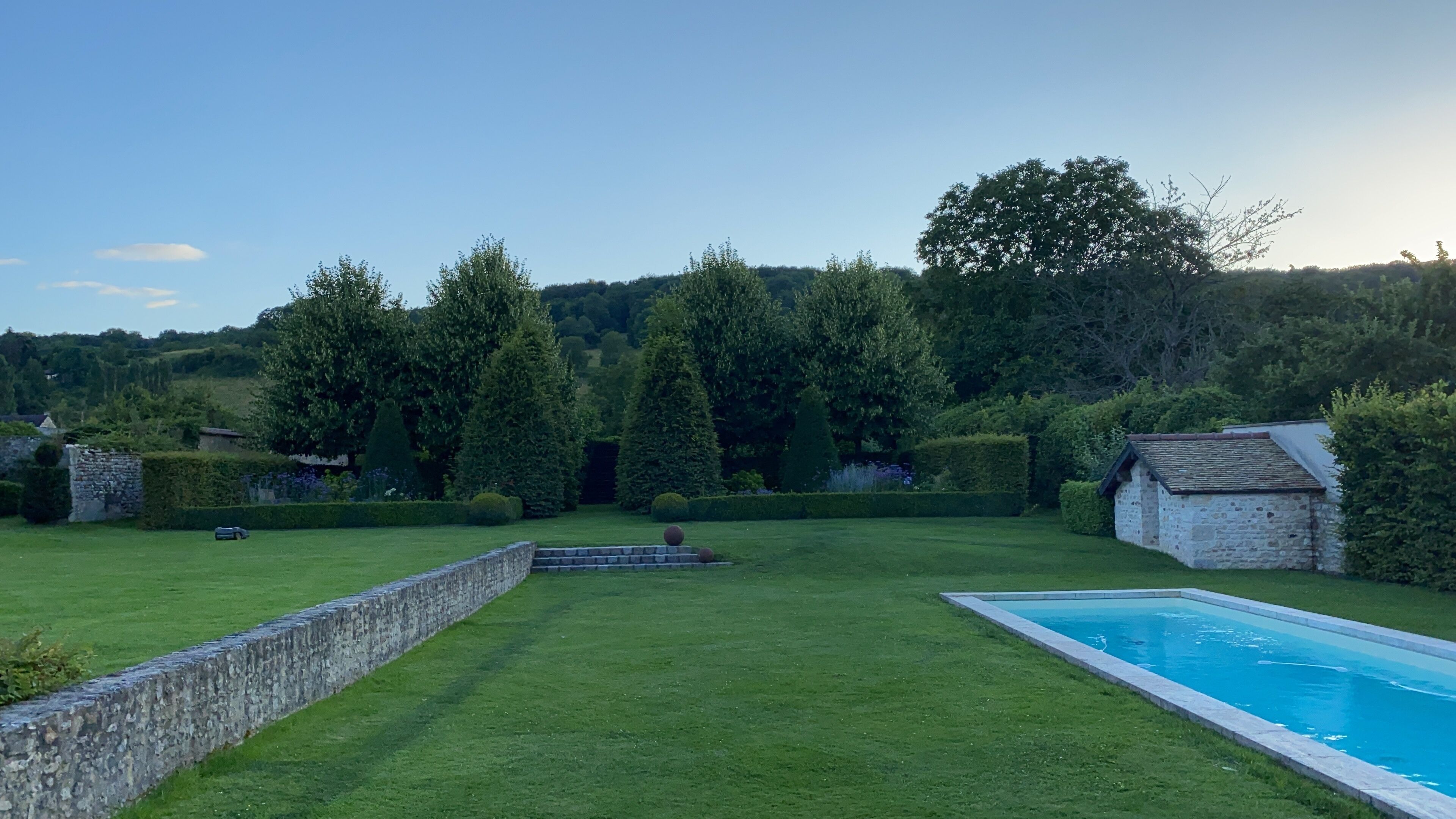 A well-maintained lawn with a swimming pool, stone walls, and a stone building.