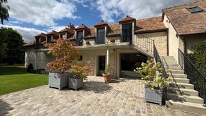 A multi-story building with a stone facade, a central entrance with a staircase, and a courtyard with potted plants. - Exceptional country apartment with pool, jacuzzi and sauna (La Chapelle-Longueville)