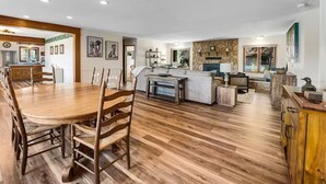 A spacious living area with a wooden dining table and chairs, a kitchen with a stone backsplash, and a fireplace. - Swan River Rendezvous - Riverfront Retreat w/Dock (Bigfork)