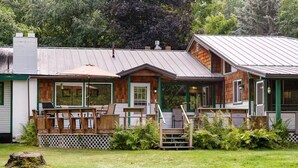 A row of cabins with a deck, a covered patio, and a small staircase leading to the entrance. - Swan River Rendezvous - Riverfront Retreat w/Dock (Bigfork)