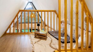 Une chambre à coucher de style loft avec un escalier en bois, une vue sur l’extérieur, un lit avec des oreillers et une petite table en bois sur laquelle est posé un livre.
