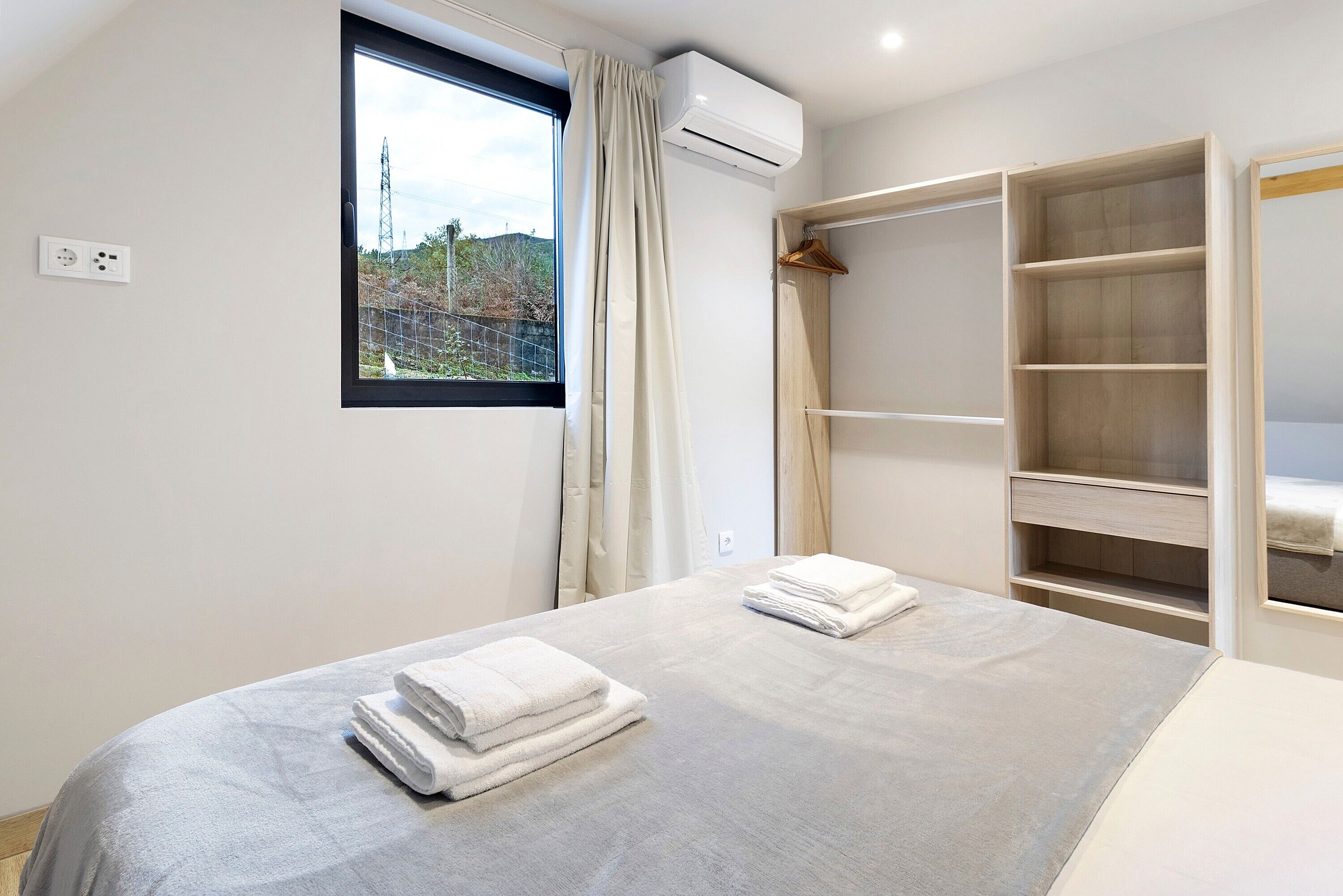 Un dormitorio con cama, ventana con cortinas, aire acondicionado y armario de madera.