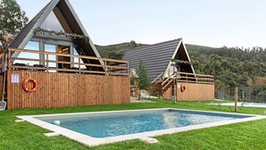 Ett modernt hus med en swimmingpool, ett trädäck och en inhägnad trädgård.