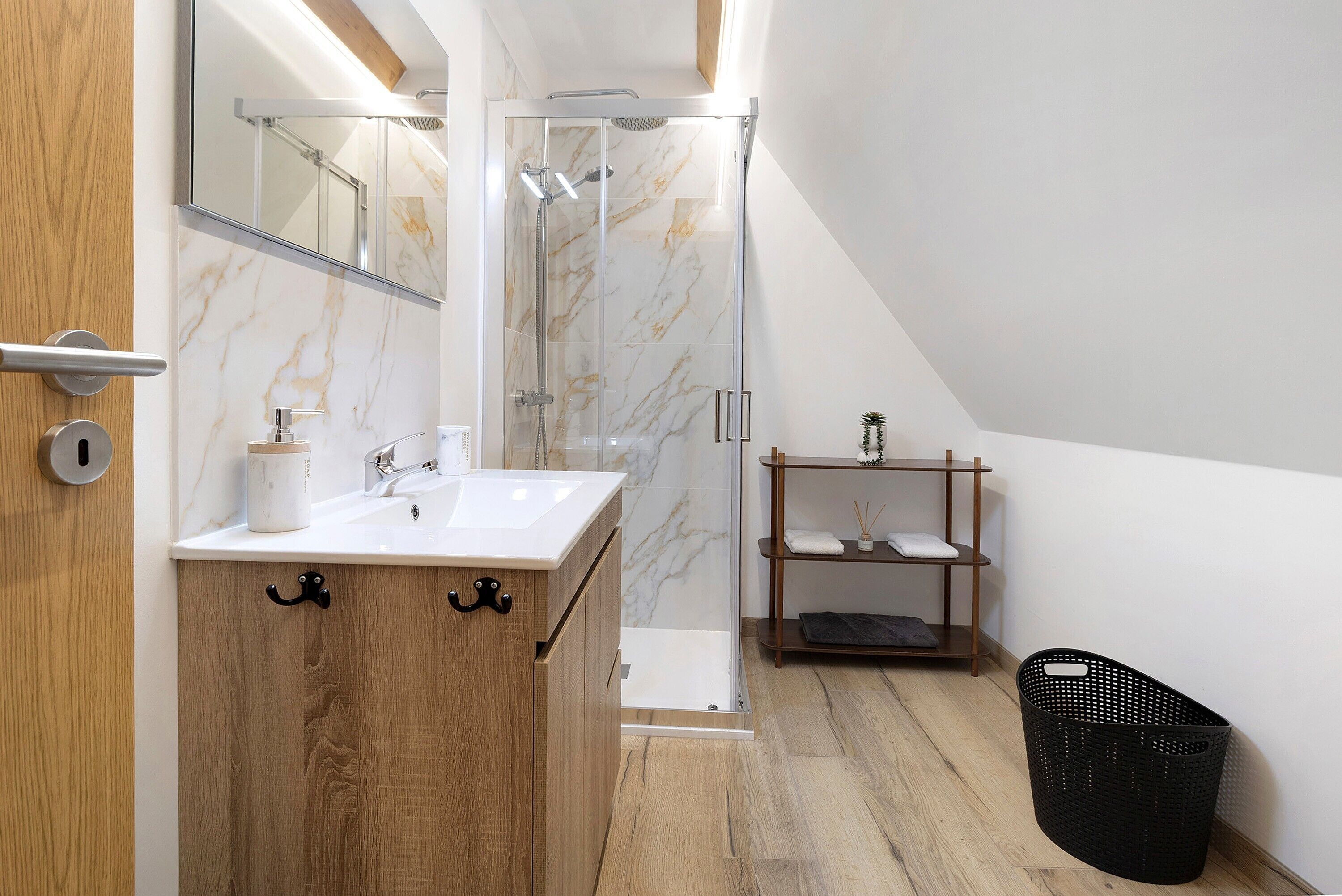 Un baño moderno con tocador de madera, cabina de ducha de vidrio y estante de madera.