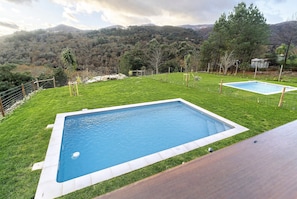 Une piscine rectangulaire entourée d’une pelouse, offrant une vue sur un paysage montagneux.