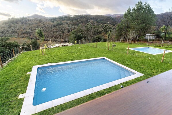 A rectangular swimming pool surrounded by a grassy area with a view of a mountainous landscape.