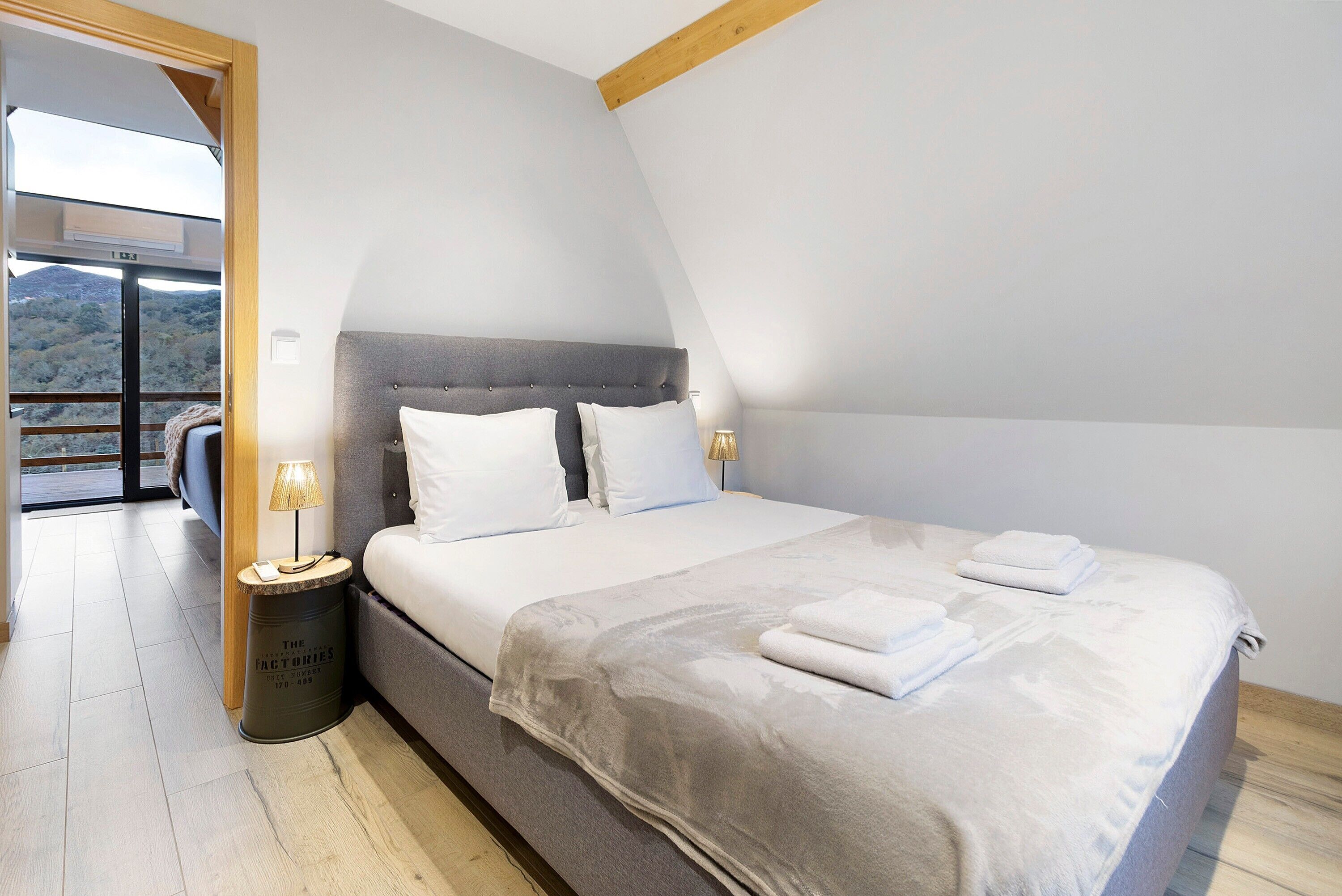 Een slaapkamer met een bed, bedlampen, een klein tafeltje en uitzicht op de omgeving.