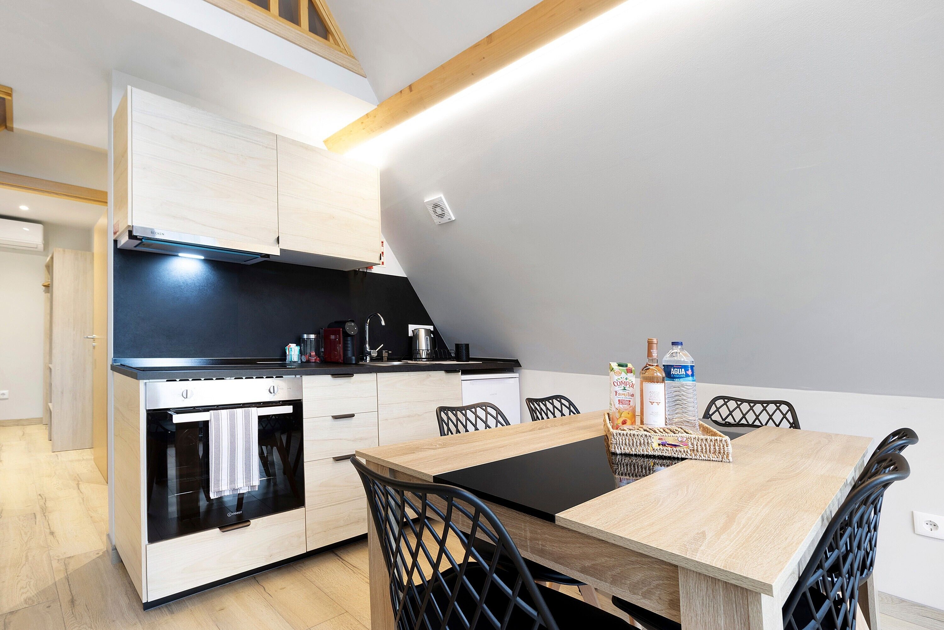 Una cocina moderna con horno empotrado, una mesa de comedor con sillas y una encimera negra.