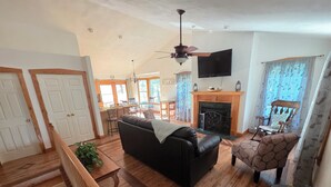 Un salón espacioso con un sofá de cuero negro, una mesa de comedor de madera, una chimenea y un televisor montado en la pared.
