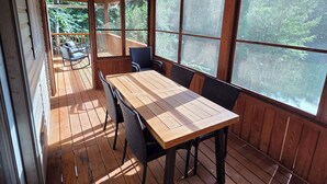 Una terraza de madera con una mesa y sillas, ventanas amplias y un ventilador de techo.