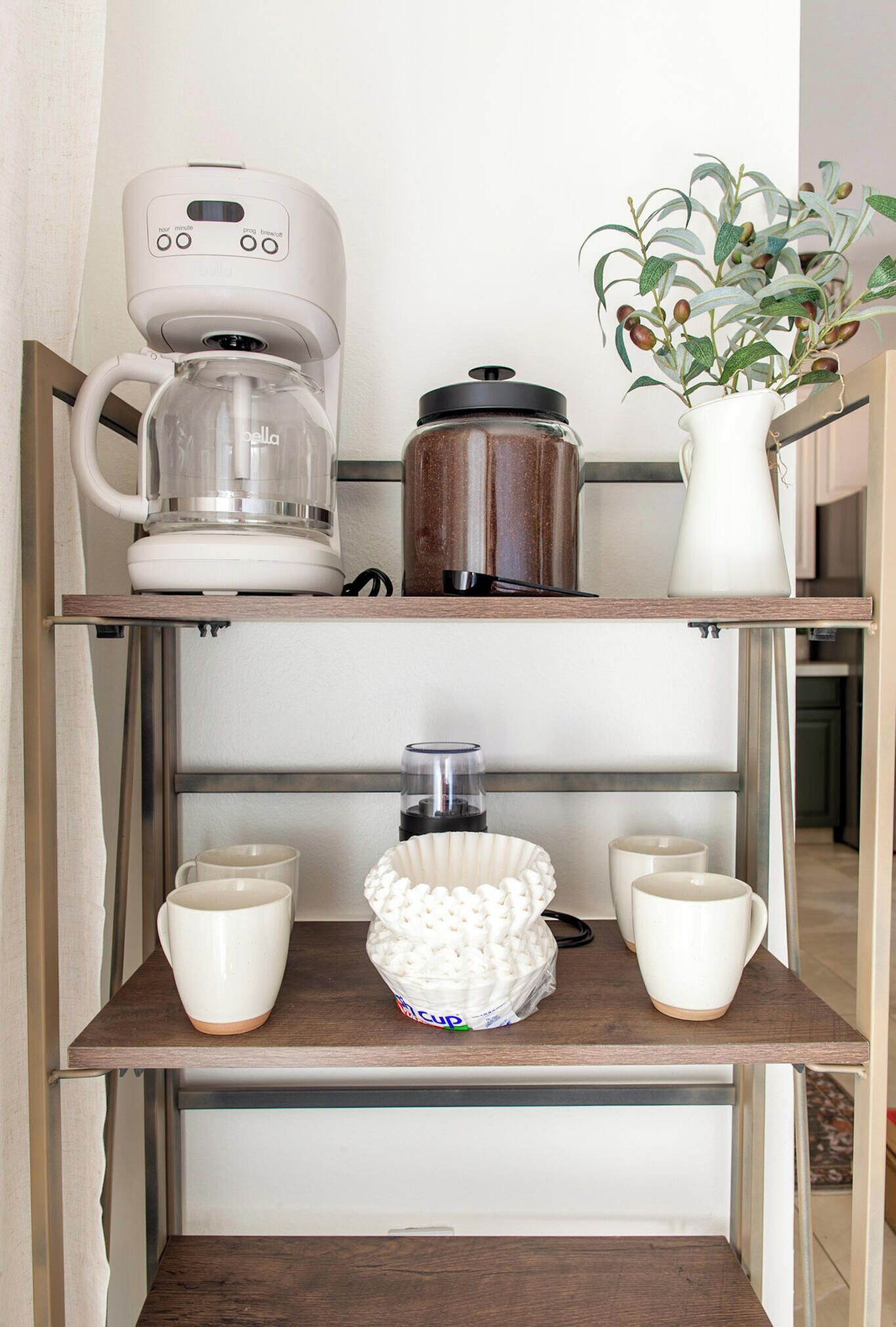 Une étagère de cuisine avec une machine à café, une casserole, un vase avec une plante et un bol de pop-corn.