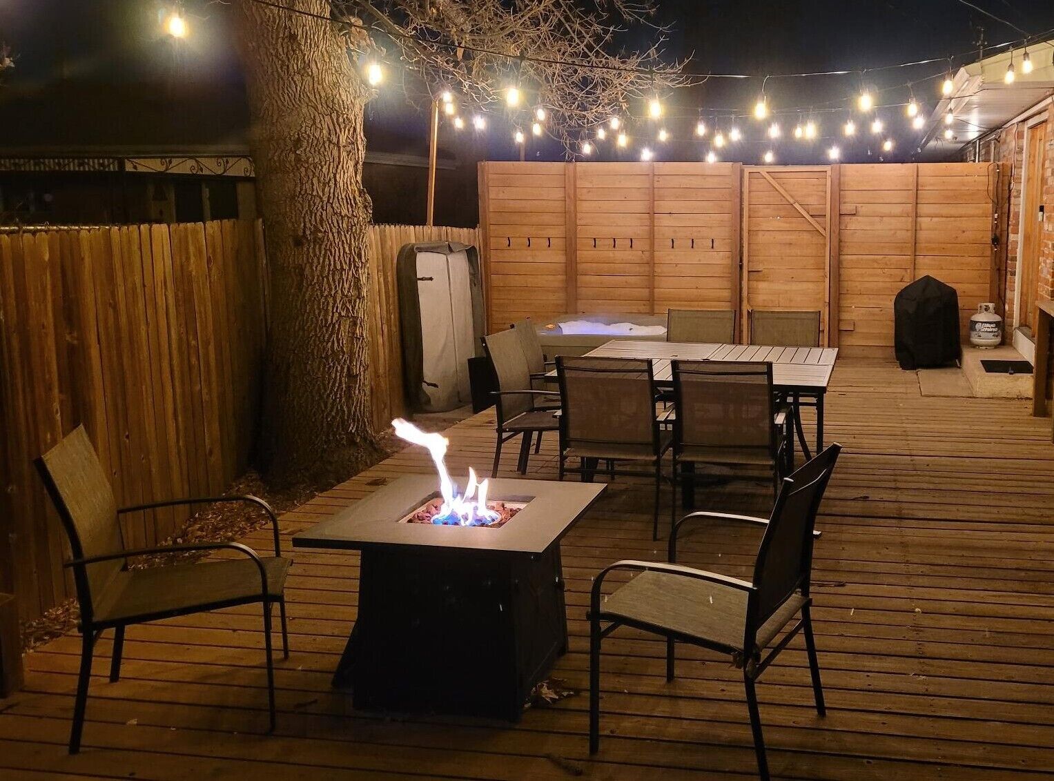 An outdoor patio with a fire pit, wooden deck, and string lights.
