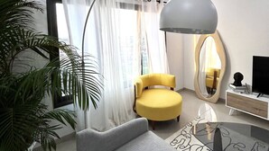 Una sala de estar moderna con un sofá, un sillón amarillo, un espejo redondo, un televisor y una planta grande en maceta.