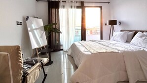 Habitación de hotel con una cama grande, un escritorio con silla, una lámpara de pie y vistas a la ciudad desde la ventana.