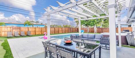 A backyard with a pergola, outdoor seating, and a pool.