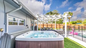A backyard with a hot tub, wooden deck, outdoor furniture, and a pergola. - Pool, Hot Tub & Putting Green Near Deerfield Beach Oasis on Fourth by Avantstay (Deerfield Beach)