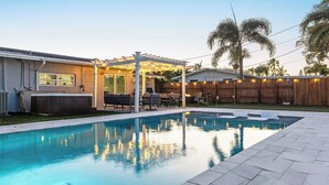 A backyard with a swimming pool, outdoor furniture, and a pergola with string lights. - Pool, Hot Tub & Putting Green Near Deerfield Beach Oasis on Fourth by Avantstay (Deerfield Beach)