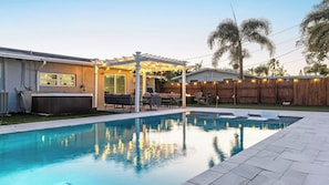 Un jardin avec une piscine, du mobilier d’extérieur et une pergola illuminée de guirlandes lumineuses.