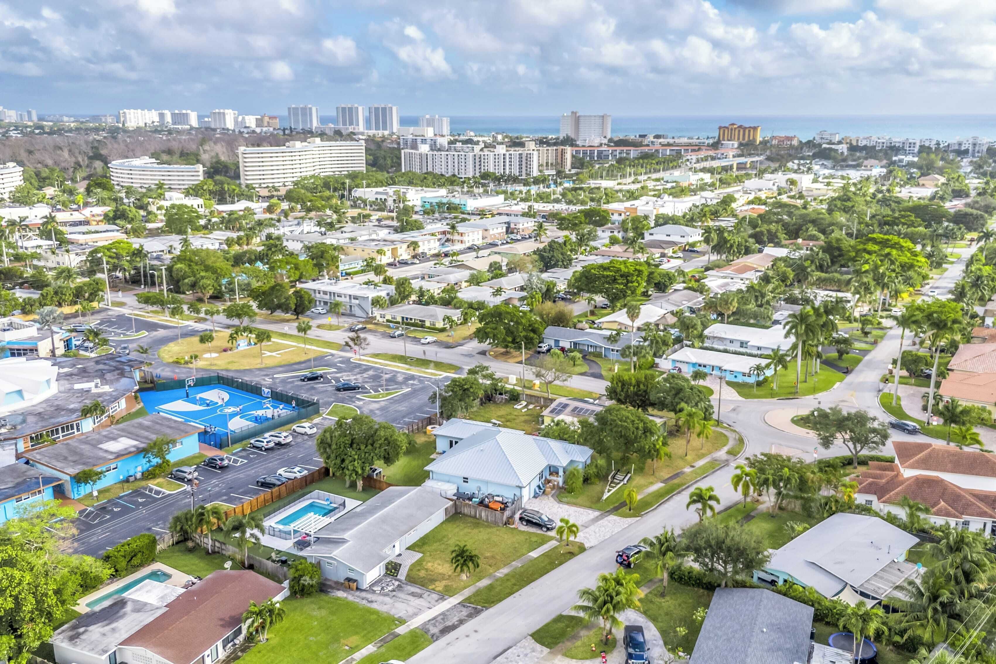 A residential area with multiple houses, a swimming pool, and a large building in the background.