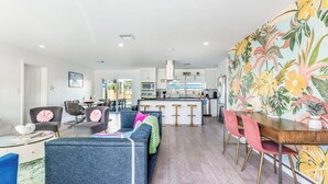 A modern kitchen with white cabinets, a central island, and a dining area with a colorful floral wallpaper. - Pool, Hot Tub & Putting Green Near Deerfield Beach Oasis on Fourth by Avantstay (Deerfield Beach)