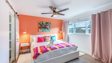 Un dormitorio con una cama, un ventilador de techo, una ventana con cortinas y un cuadro en la pared.