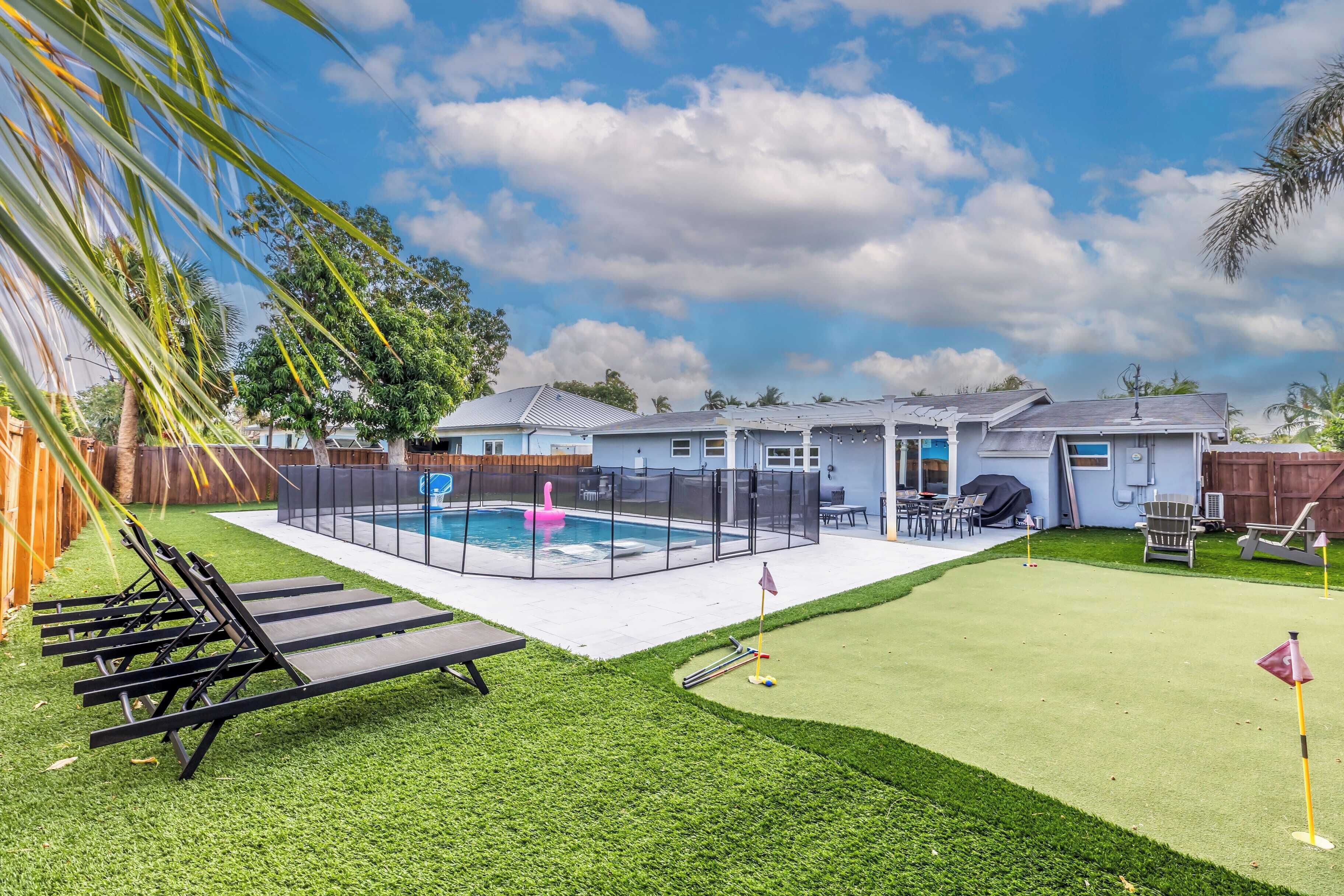 A backyard with a pool, artificial grass, and a fenced play area.