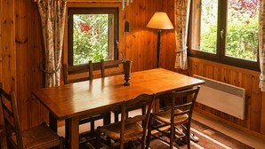Een houten chalet interieur met een eettafel, stoelen, een hanglamp en ramen met gordijnen.