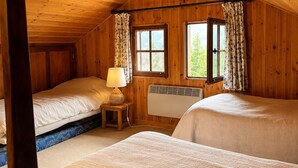 Een slaapkamer in een chalet, met twee bedden, een klein tafeltje met een lamp, een raam met gordijnen en een houten plafond.